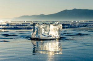 Bloc de glace isolé fondant sur un lac gelé avec les montagnes en arrière-plan